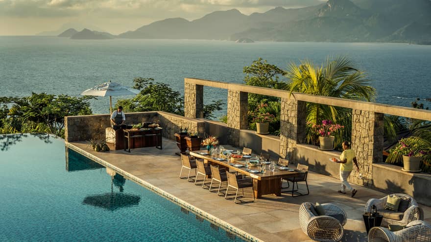 Aerial view of Four-Bedroom Residence Villa private deck with 8-person dining table beside pool, ocean view