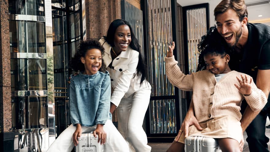 A family playing with suitcases outside of a building.