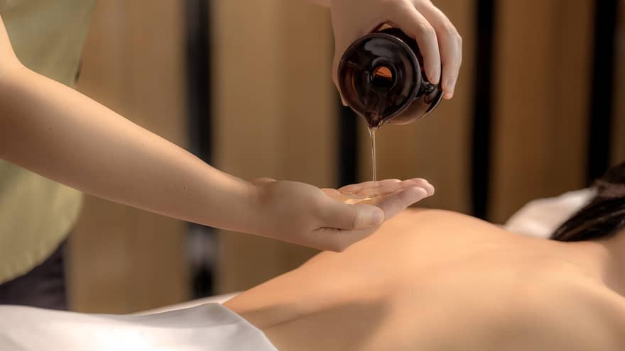 Spa therapist pours oil into hand above woman?s bare back in preparation for a massage