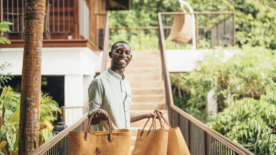 Person in linen shirt standing on catwalk holding four orange tote bags