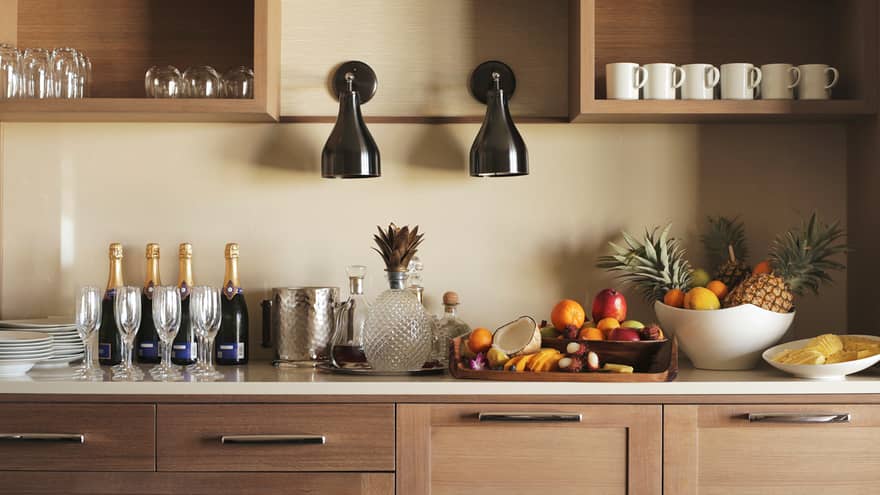 Close-up of Club Floor kitchenette bar and wood cabinets with Champagne and glasses, fresh fruit in baskets