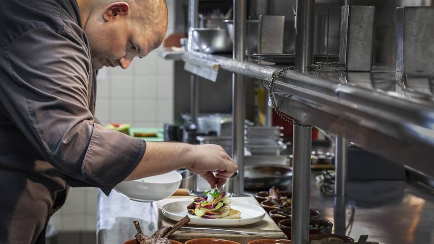 Chef garnishes gourmet meat entree on steel kitchen line