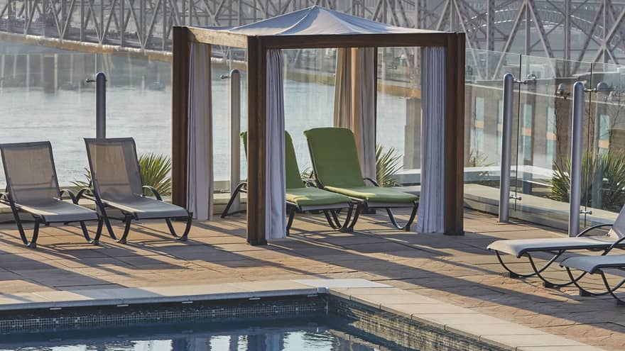 An outdoor swimming pool area, featuring sun lounge chairs, a cabana on deck, and surrounded by clear waters.