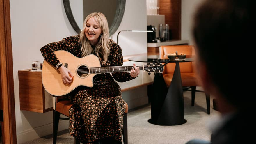 Woman sings a song with a guitar for guests in a hotel suite