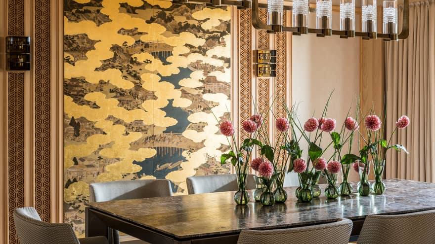 Elegant dining area with a large table decorated with pink flowers in small vases and a gold-accented wall panel