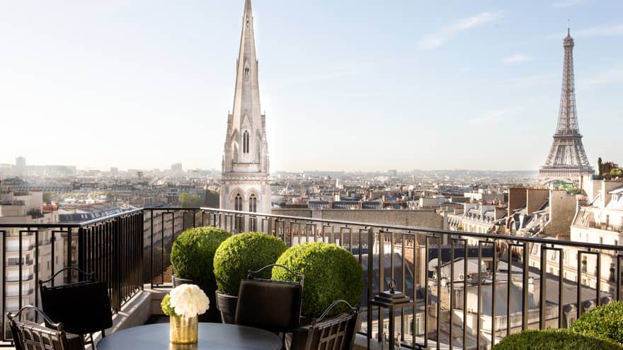 Patio dining table with white roses, potted shrubs iron balcony overlooking Paris rooftops, cathedrals