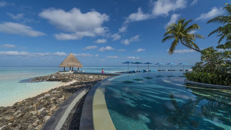 A curving pool lined with umbrellas that connects to a hut overlooking the ocean
