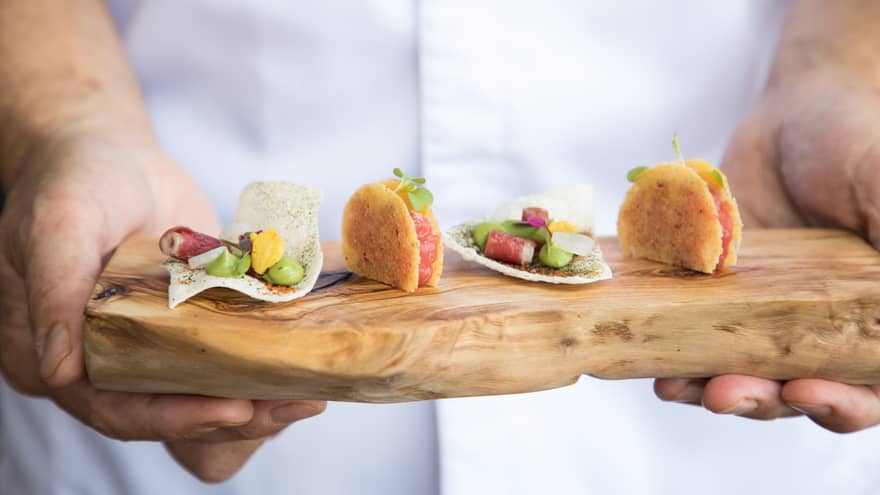 Close-up of hands holding rustic wood platter with little gourmet crackers with seafood, sauce