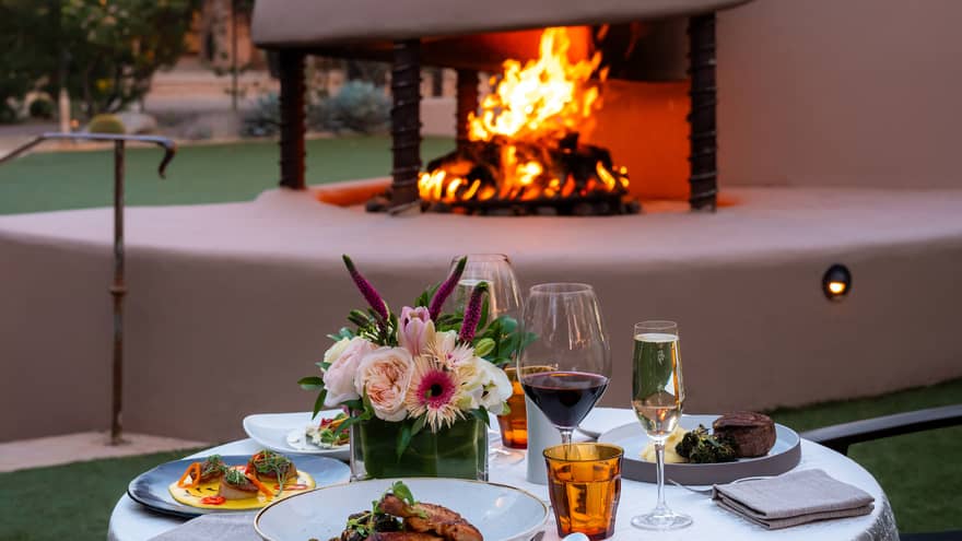 An outdoor dining table set with dishes and glasses near a fire pit