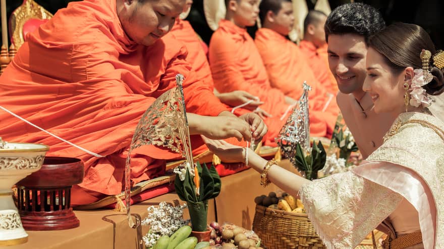 Bride and groom at traditional Thai wedding ceremony, monk ties bracelet around woman's wrist
