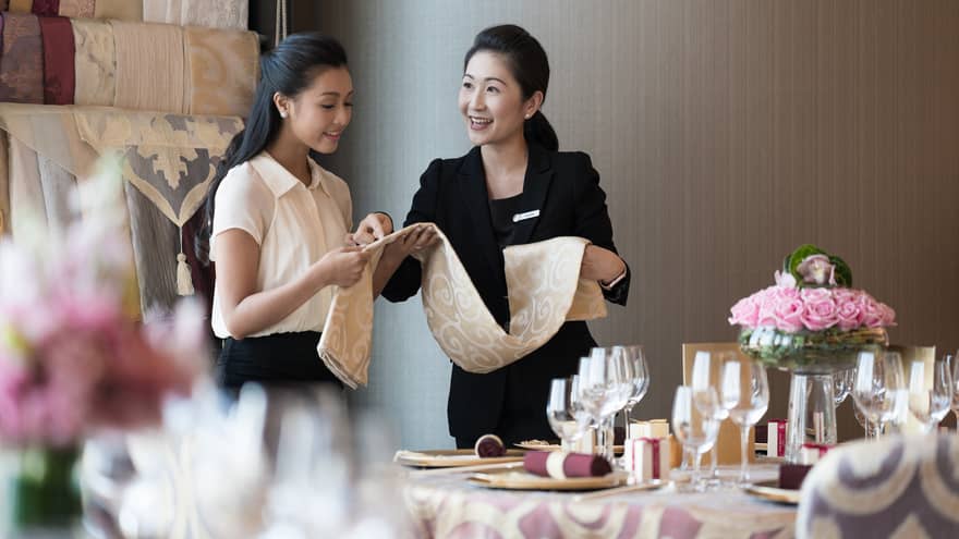 Two people examine table linens selection at small dining table