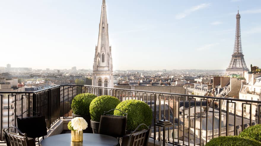 Patio dining table with white roses, potted shrubs iron balcony overlooking Paris rooftops, cathedrals