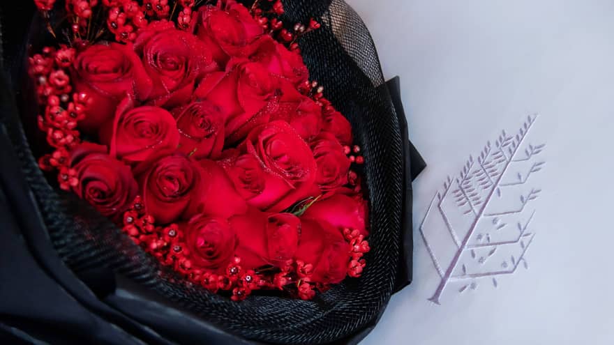 Bouquet of red roses wrapped in black fabric laying on a white pillow with the Four Seasons logo