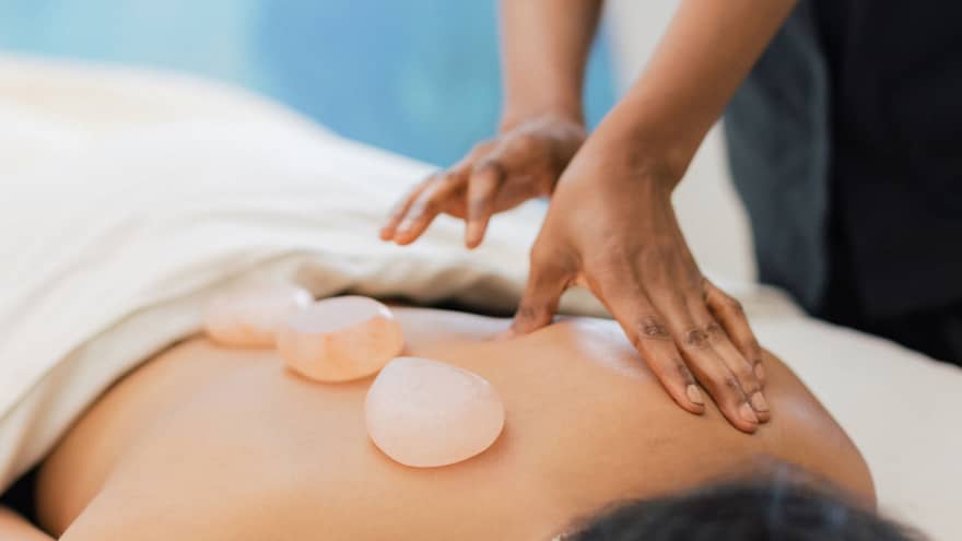 Masseuse places salt stones on a person's bare back