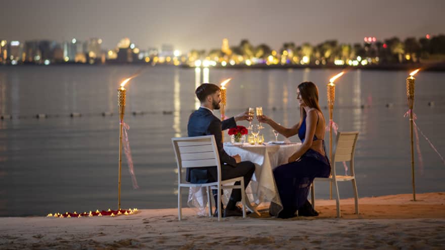 A couple dines along the gulf with the Doha city skyline in the background.