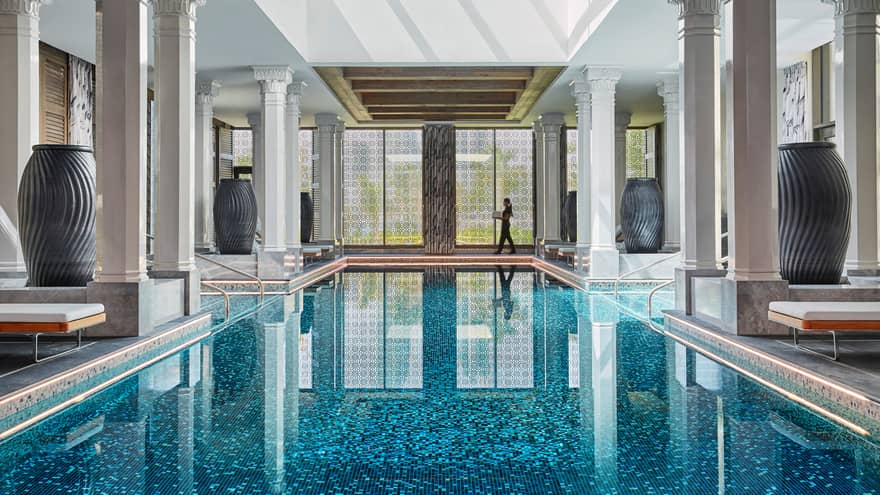 Sunny indoor swimming pool lined with tall black vases, white pillars