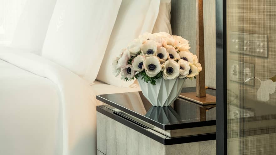 White flowers in modern vase on nightstand beside hotel bed
