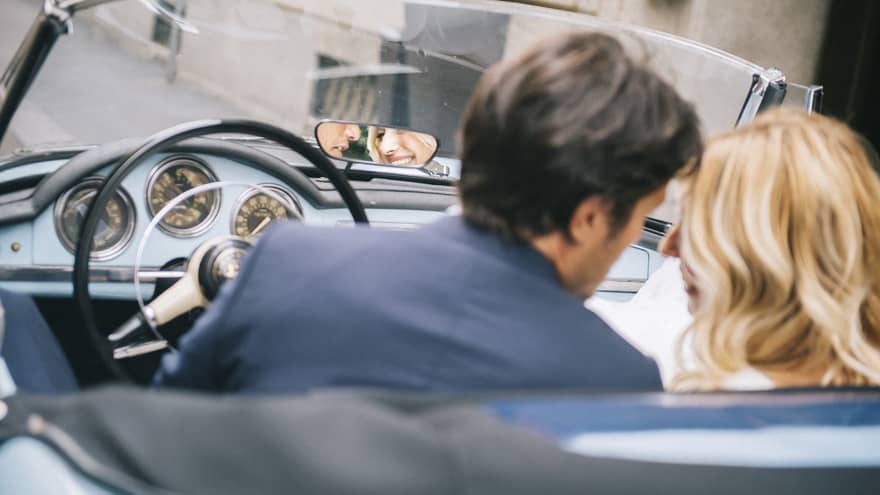 Couple sitting in front seats of classic convertible car lean in close
