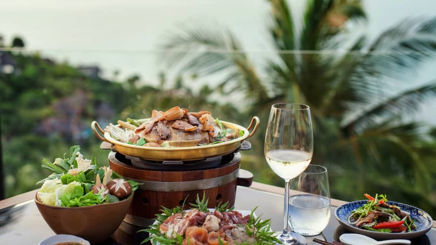 Four plates of food, glass of water and white wine, tropical scenery in background