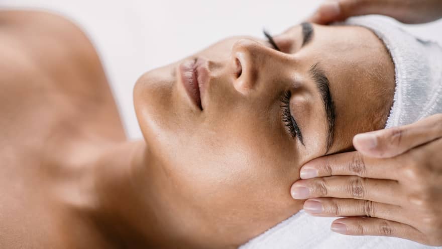 Hands massage woman's temples as she closes her eyes, spa towel around hair