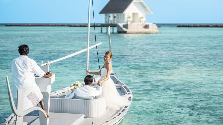 Bride and groom head toward their overwater wedding venue in traditional Maldivian boat