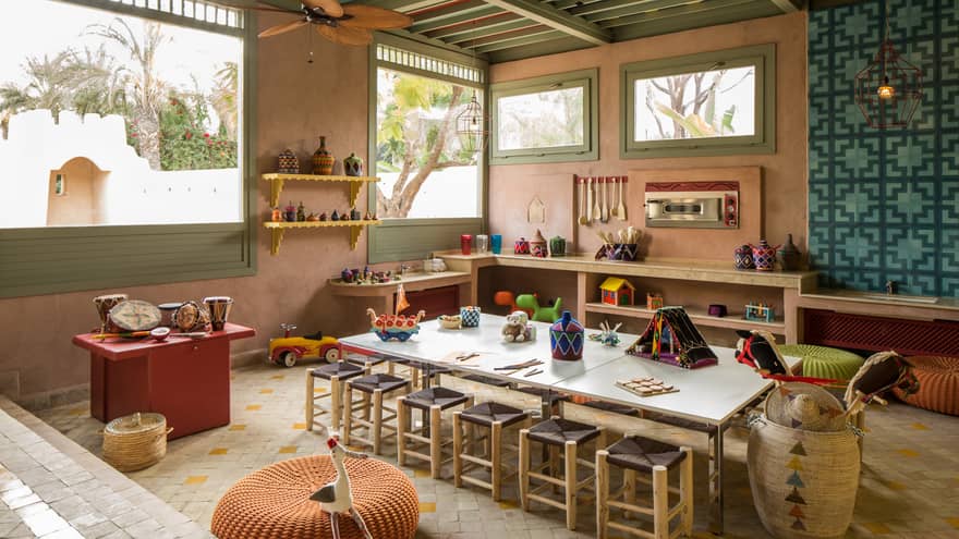 Kids Club long craft table with stools, toys on shelves along wall under sunny windows