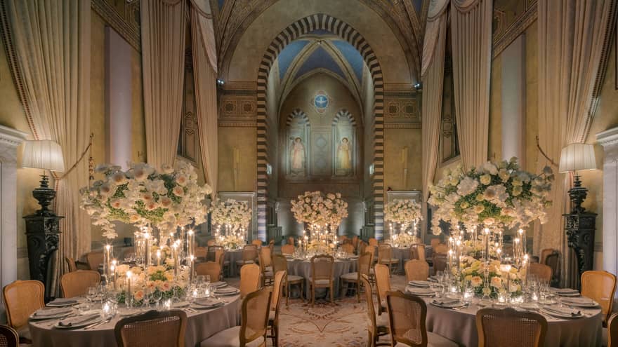 Grand dining room with tall arched ceilings and round elegantly set tables with tall white flower centrepieces
