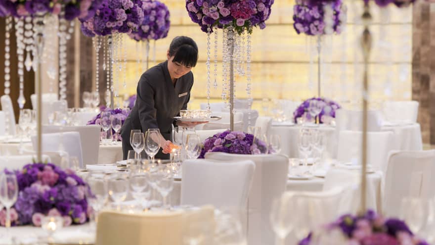 Staff sets banquet tables with tall purple flower centrepieces in Topaz Room