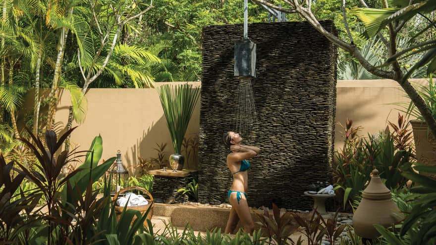 Woman in bikini rinses off under outdoor rain shower