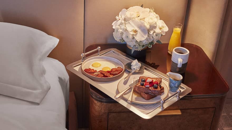 Tray on nightstand with eggs, bacon and french toast on it.
