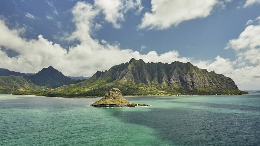 Sweeping green Oahu, Hawaii mountains, small island over turquoise lagoon, white clouds