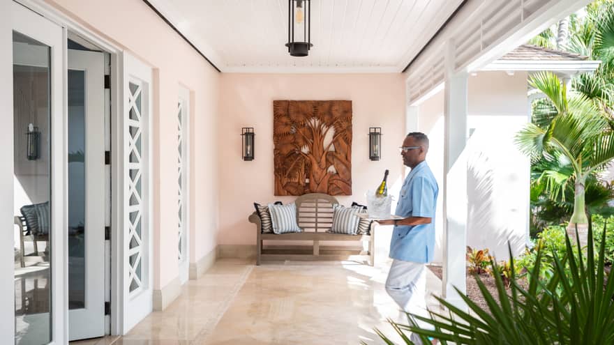 Villa butler carries bucket of ice with Champagne bottle through sunny villa
