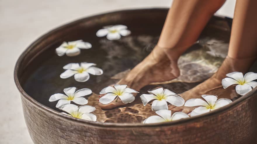 A woman's feet in a bowl of water and flowers.