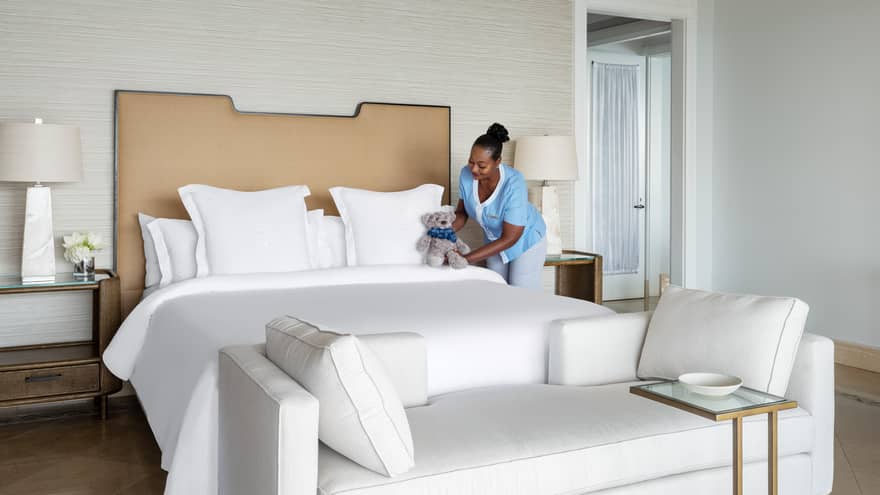 Hotel staff sets teddy bear on bed in front of plush bench in Beachfront Villa Residence bedroom