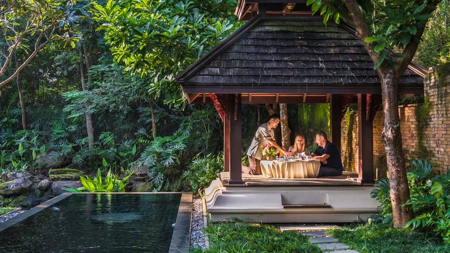 Hotel staff pours fresh juice for couple at private patio dining table under wood gazebo
