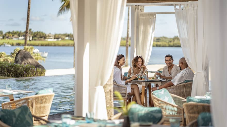 Four friends dine poolside at Bambou under a cabana