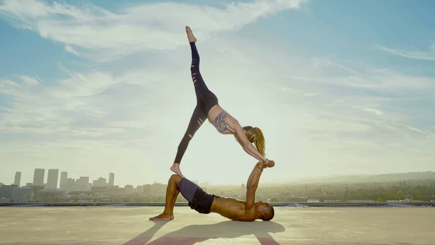 Helipad yoga pose, woman with leg in air balances on top man laying on ground on helicopter pad