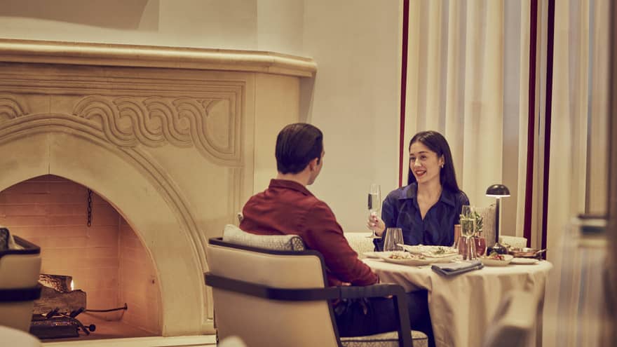 A couple enjoys champagne and a candlelit dinner by an ornate fireplace