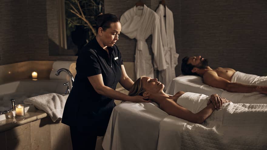 Two guests laying on massage tables in a room with a spa tub.