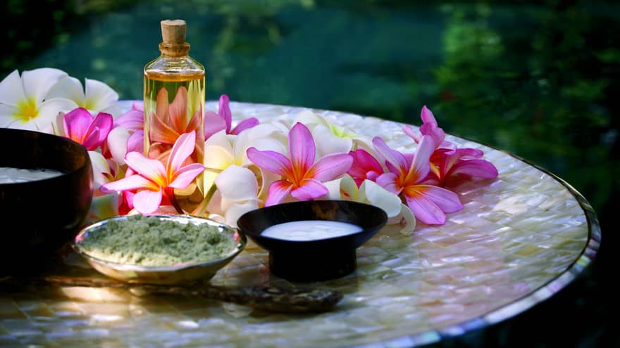 Spa tray with fresh pink and white flowers, glass bottle with oil and cork, small bowls of salt and lotion