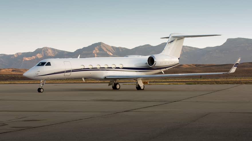 Private jet parked on a runway with mountain range in the background.