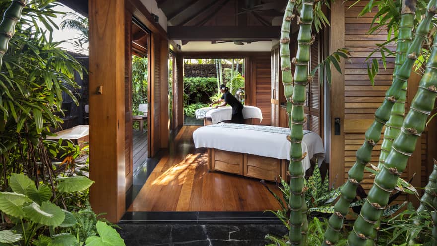 Spa staff spreads sheet on couples massage beds on open-air pavilion