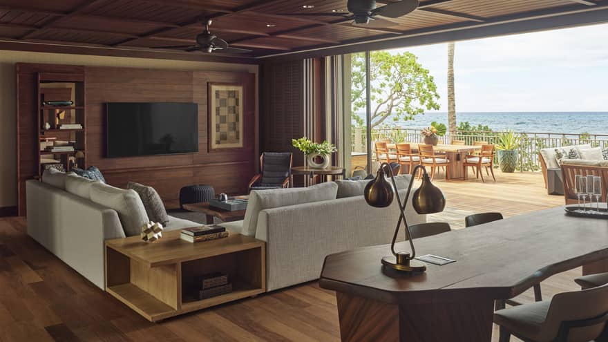 Wooden desk and living room with light grey sofa, full wall of windows with ocean view