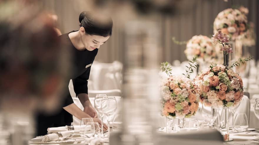Hotel server sets formal banquet table with pink roses, flower arrangements