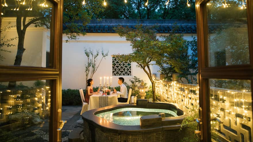 View past hot tub to couple dining at candlelit table on patio with lights