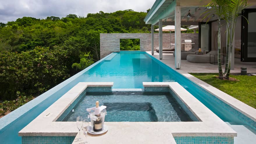 Champagne, two glasses on edge of residence whirlpool, long outdoor swimming pool