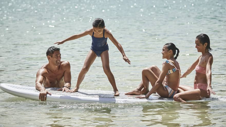 A family sitting on a large surf or paddleboard.
