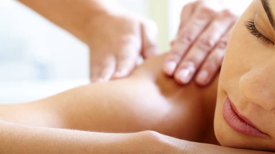 Close-up of woman's face with eyes closed, bare shoulder as she gets a Balinese massage