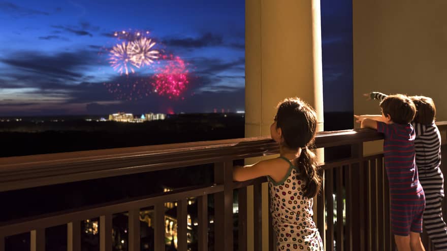 Young girl stands on Four Seasons Hotel balcony, watches colourful fireworks display over Walt Disney World resort