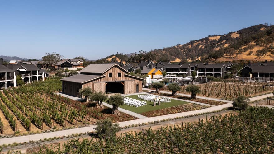 A farmhouse with mountains in the background and rows of greenery all around.
